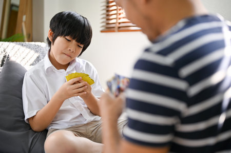 Playful and happy young Asian son playing a kid's board game or a kid's card game with his dad in the living room. family fun time conceptの写真素材