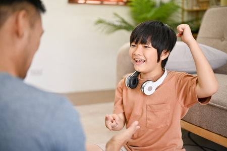 Cute and happy Asian little boy playing rock paper scissors with his dad, spending fun family games time in the living room together.の写真素材