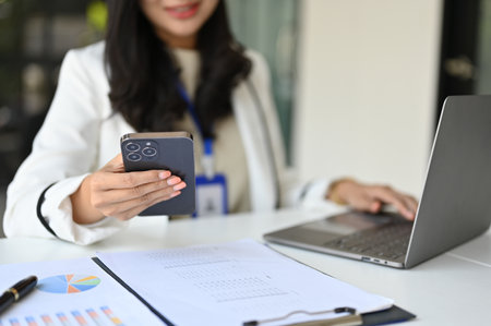 Cropped image of a professional and successful millennial Asian businesswoman or female CEO using her phone while working at her desk.の写真素材