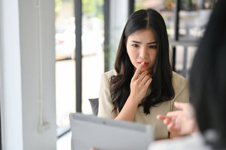 Stressed and thoughtful millennial Asian woman having a serious talk with her personal financial consultant.の写真素材