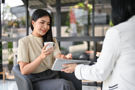 Attractive and gorgeous millennial Asian female CEO having an informal meeting with her secretary in the office.の写真素材