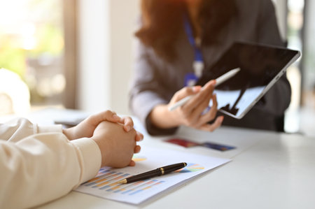 Professional Asian female banker or financial consultant showing something on tablet screen to her client while planning an investment plan together in the office.の写真素材