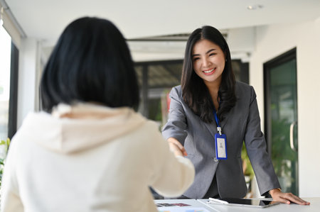 Attractive and charming millennial Asian businesswoman or female banker shaking hand with her business client in the office.の写真素材