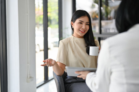 Smiling and gorgeous millennial Asian female CEO or executive manager discussing about a new project with her employee in her office.の写真素材