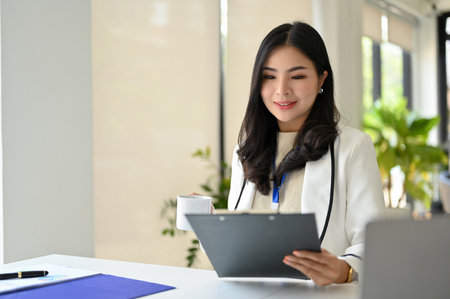 Professional and confident millennial Asian businesswoman reading and reviewing business report, working at her desk in her private office.の写真素材