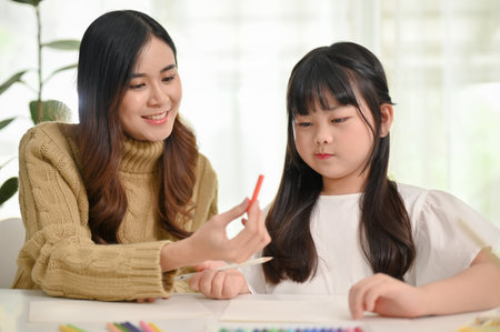 Happy and caring Asian mom enjoys spending creativity time with her little daughter at home, drawing and painting together.の写真素材