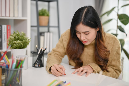 Focused young Asian woman drawing and painting on paper with oil pastel color. leisure and hobby conceptの写真素材