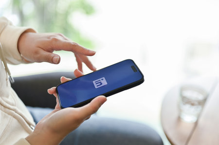Chiang Mai, Thailand - March 31 2023: A woman in casual clothes relaxes sitting in a cafe and using LinkedIn application on her phone. iPhone with LinkedIn logo on screen. side viewのeditorial素材