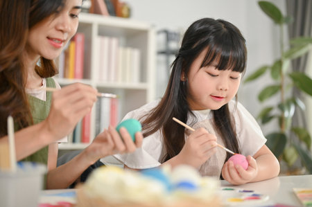Cute little Asian girl painting Easter eggs with her mother in the living room. Festive holiday conceptの写真素材