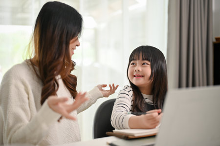An adorable young Asian girl enjoys talking with her mother while doing fun activity at home together.の写真素材