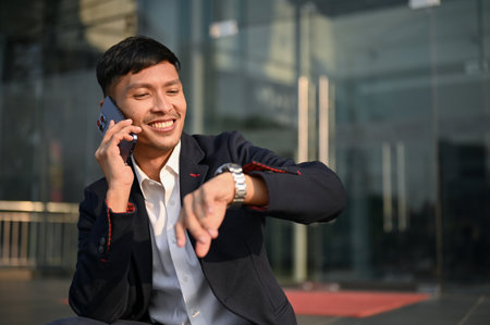 Attractive and happy millennial Asian businessman or male banker talking on the phone with someone...