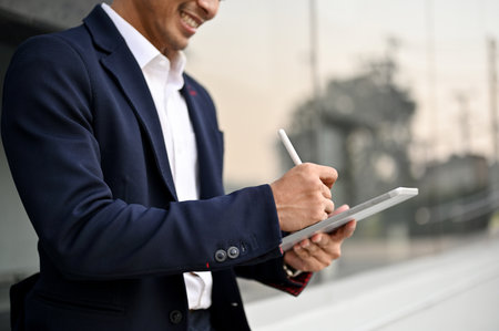 Side view close-up image of a handsome millennial Asian businessman in a business suit using his tablet while walking in a city. Urban lifestyle conceptの写真素材