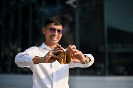 Stressed and broke millennial Asian businessman opening his empty wallet in the city. bankrupt,...
