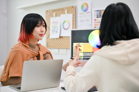 Focused and talented young Asian female graphic designer planning a new design project with her colleague in the studio. co-working and teamwork conceptの写真素材