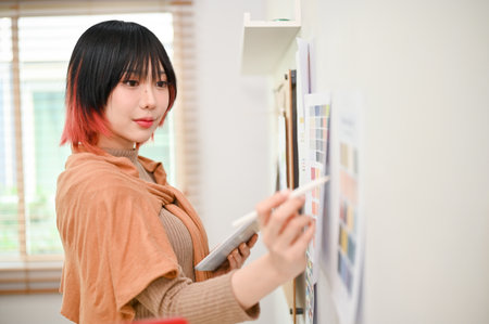 Inspired and talented young Asian female graphic designer working on her new design project in her studio and choosing color from color swatch sample.の写真素材
