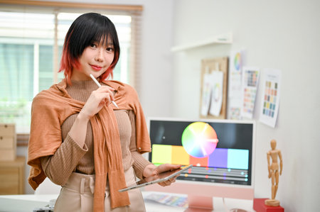Portrait of a smiling and pretty young Asian female web graphic designer or interior designer stands in her studio with her digital tablet.の写真素材