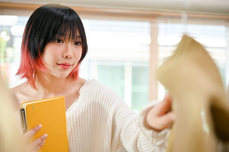 Beautiful young Asian female fashion clothes shop seller checking the quality and stock of her new clothes collection, working from home. small business conceptの写真素材