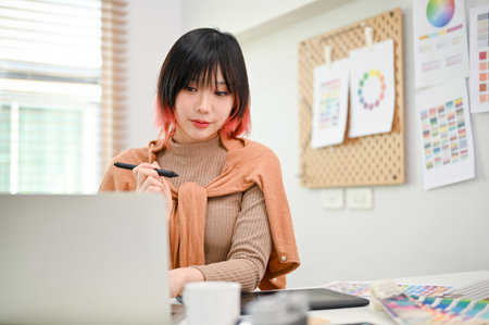Charming young Asian female graphic designer working on her new design project on laptop in her studio.の写真素材