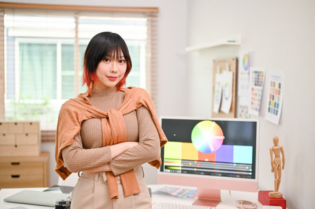 Portrait of a smiling and talented young Asian female web graphic designer or interior designer stands in her studio with arms crossed.の写真素材