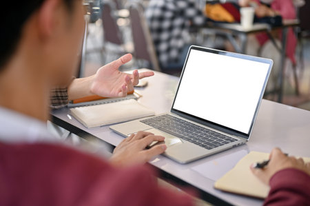 Close-up image of a young Asian male college student using laptop and doing a group project with his friends. laptop white screen mockupの写真素材