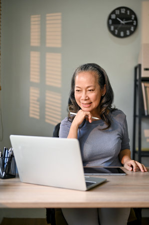 Portrait of a professional and attractive Asian-aged businesswoman or female boss working on her business tasks on laptop in her private office.の写真素材