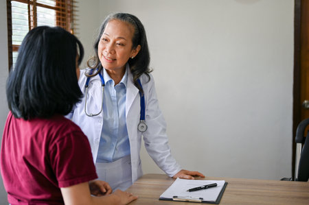 Professional senior Asian female doctor consulting a medical treatment plan with a patient in the examination room at a clinic.の写真素材