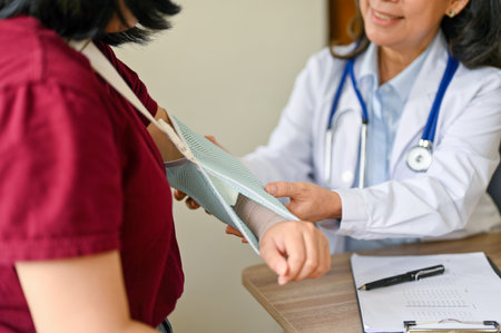 Close-up image of a female patient with a broken arm is being checked and diagnosed by an orthopedic doctor in the examination room at a hospital. Health care and medical conceptの写真素材