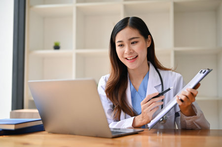 Attractive and smart millennial Asian female doctor having an online medical webinar with her team or counseling through video call with her patient.の写真素材