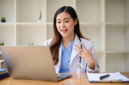 Professional millennial Asian female doctor is having online medical counseling with her patient or a meeting with her team. Health care and technology conceptの写真素材