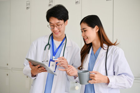 Smart young Asian male doctor or medical student discussing his medical cases, looking at tablet screen together with a female colleague during the coffee break.の写真素材