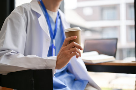 Cropped image of a male doctor sits in a cafe holding a takeaway coffee cup, having a quick lunch break at a coffee shop.の写真素材