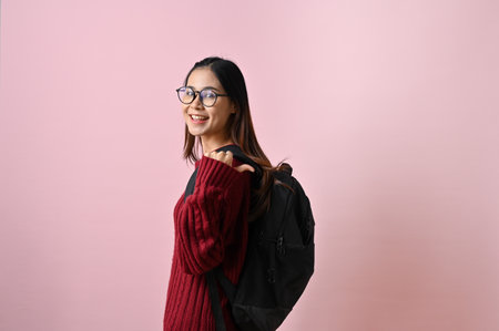 Pretty and smiling young Asian female college student in a red knitted sweater and glasses stands...