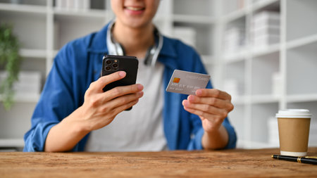 Close up view of young man doing an online shopping with smartphone while sitting in living room.