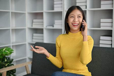 Young attractive Asian woman having a phone call with her friends while sitting on the sofa at home.の写真素材
