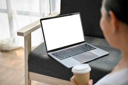 Close-up image of a happy senior woman sipping coffee and using her laptop on sofa in her living room. laptop computer white screen mockupの写真素材