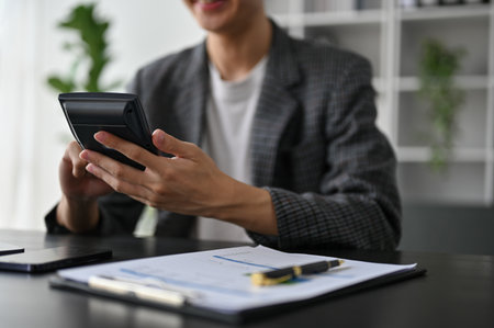 Close up view of young smart businessman using calculator while working in the office room.の写真素材