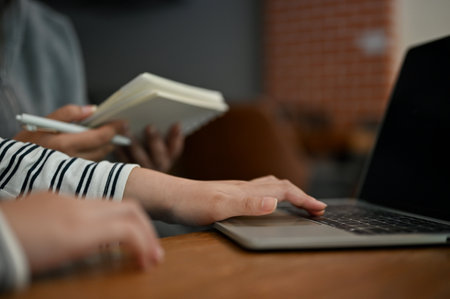 Cropped image of an Asian female college student talking with her friends, using laptop computer,...