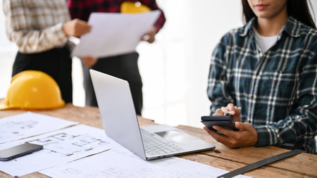 Close-up image of an Asian female engineer measuring and checking building layout, using scientific calculator, and working in the office.の写真素材