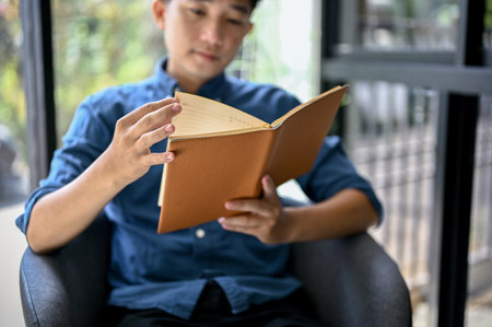 Close-up image, Happy millennial Asian man reading a book while relaxing in a coffee shop. leisure and hobby conceptの写真素材