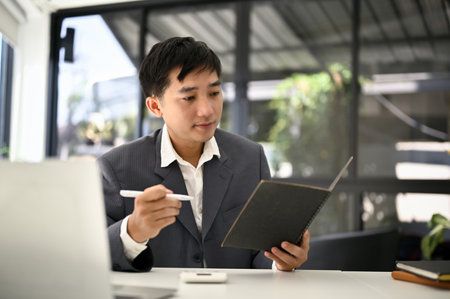 A professional Asian businessman checks his meeting schedule on his planner book at his desk in the office.の写真素材