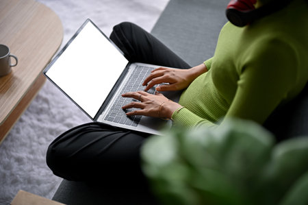 Close-up image of a woman in casual comfy clothes using her laptop computer on a sofa in a living room. laptop white screen mockupの写真素材