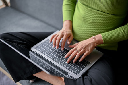 close-up image of a young Asian woman in casual clothes typing on keyboard, using her laptop computer on a sofa in her living room. work from home conceptの写真素材