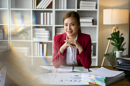 Successful and attractive millennial Asian businesswoman or female boss in a formal business suit sits at her desk in the office.の写真素材