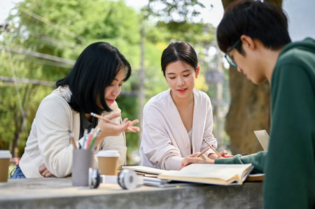 Beautiful young Asian female college student focuses on listening to her friend explain math while preparing for the exam at a campus park together.の写真素材