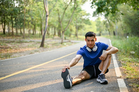 Handsome and fit Asian man in sportswear is stretching his leg on the street at a park, cooling down after exercise, or warming up before running.の写真素材