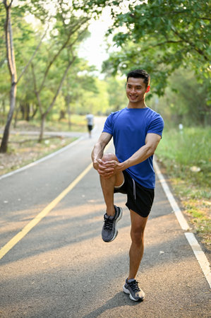Portrait of a happy and handsome millennial Asian man in sportswear stretching his leg on a street before running.の写真素材