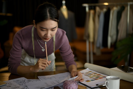 Professional millennial Asian female fashion designer or tailor focuses on designing and sketching new costume models in her studio.の写真素材