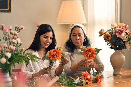 Attractive young Asian woman joining fresh flower arrangement workshop with her mother. Hobby and family time conceptsの写真素材