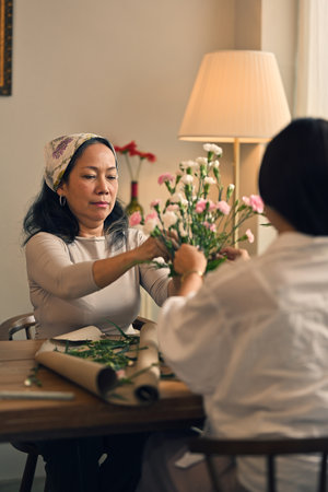 Portrait of a beautiful retired Asian woman focuses on arranging a vase with fresh flowers in a workshop. Lifestyle conceptの写真素材