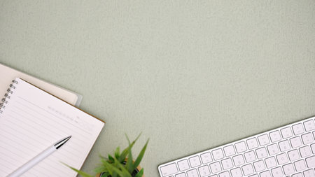 Top view, Office workspace with pc keyboard, pen, notebook, and empty space on green background.